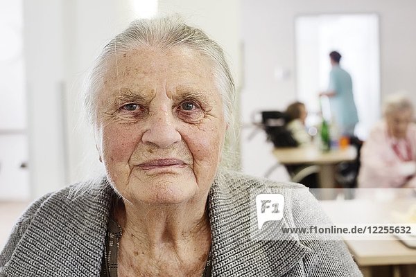 Demente Seniorin in einem Altenheim  unscharfes Pflegepersonal im Rücken  Deutschland  Europa