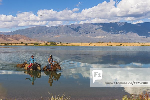 Nomad kids on horses crossing the Tuul river during summer time  Gorkhi-Terelj National Park  Mongolia  Asia