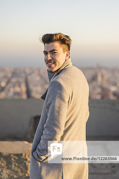 Portrait of smiling young man wearing grey coat at sunset