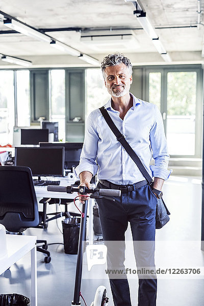 Portrait of smiling mature businessman with scooter in office