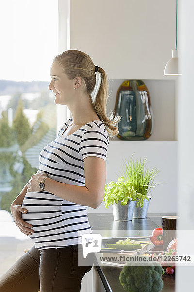 Lächelnde schwangere Frau  die zu Hause in der Küche steht.