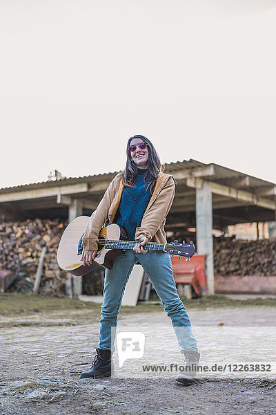 Smiling young woman holding guitar outdoors on a farm
