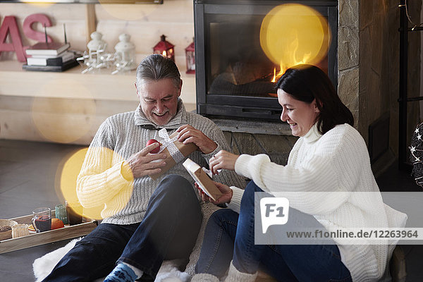 Glückliches reifes Paar am Kamin beim Auspacken von Geschenken