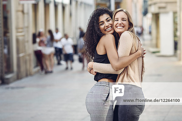 Porträt zweier glücklicher Freunde  die sich auf der Straße umarmen