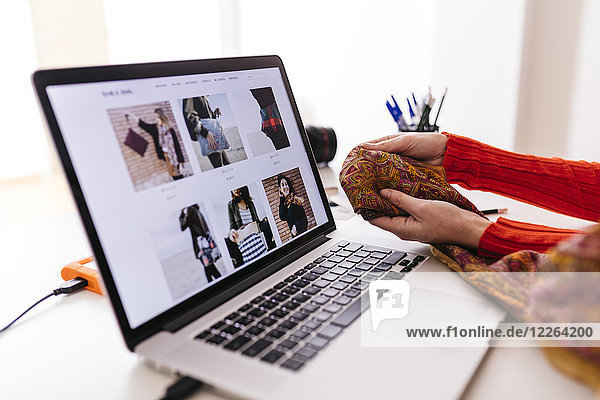 Close-up of fashion designer in studio with laptop examining fabric