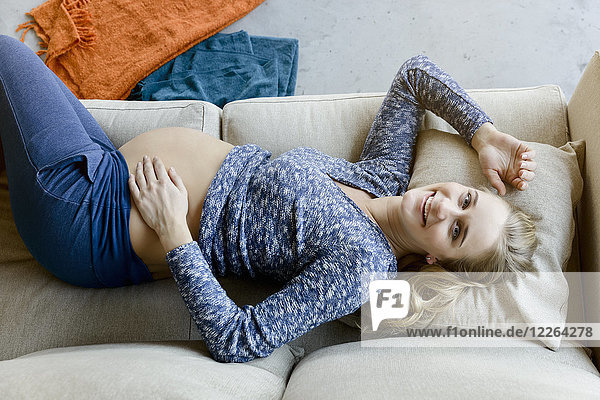Porträt einer glücklichen Schwangeren  die zu Hause auf der Couch liegt.
