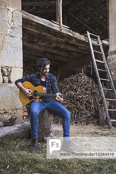 Junger Mann spielt Gitarre im Freien auf einem Bauernhof