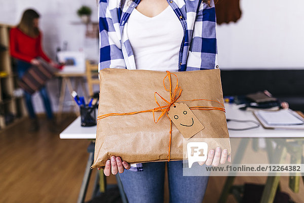 Close-up of fashion designer holding a wrapped package in studio with smiley face