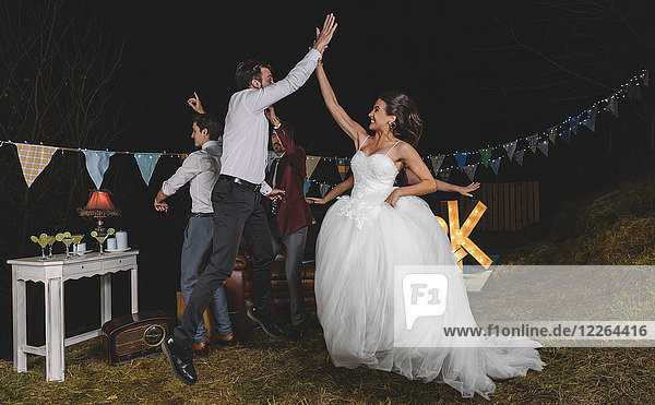 Fröhliches Brautjumping und High Five mit jungem Mann auf einer Nachtfeldparty mit Freunden