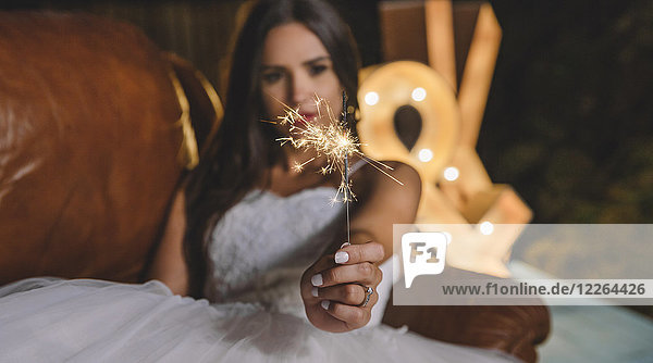 Close-up of sparkler in the hand of a bride lying on sofa on a night party outdoors