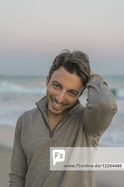 Porträt des lächelnden jungen Mannes am Strand bei Dämmerung