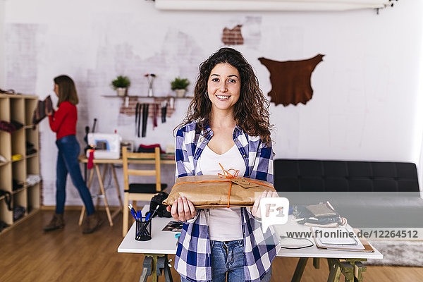 Smiling fashion designer holding a wrapped package in studio