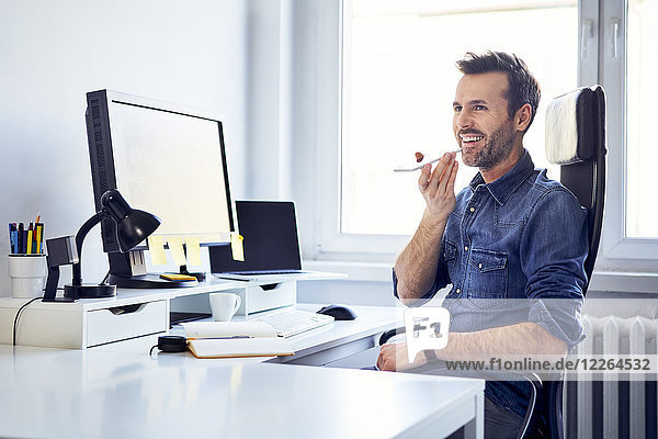 Lächelnder Mann mit Smartphone am Schreibtisch im Büro