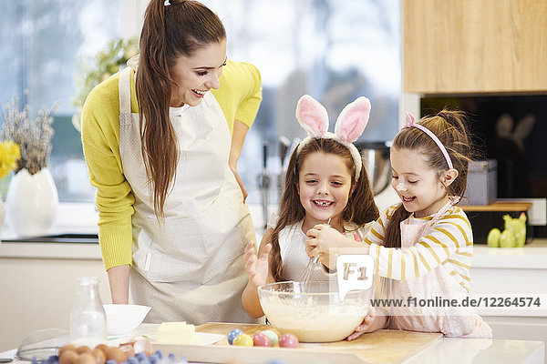 Glückliche Mutter und Töchter backen gemeinsam Osterkekse in der Küche