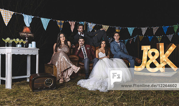 Porträt des Hochzeitspaares mit Freunden auf dem Sofa auf einer Nachtfeld-Party