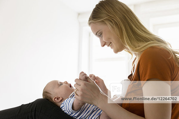 Smiling mother holding baby boy in lap on bed