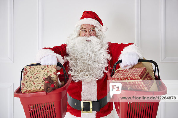 Porträt des glücklichen Weihnachtsmannes mit zwei Einkaufskörben und Weihnachtsgeschenken