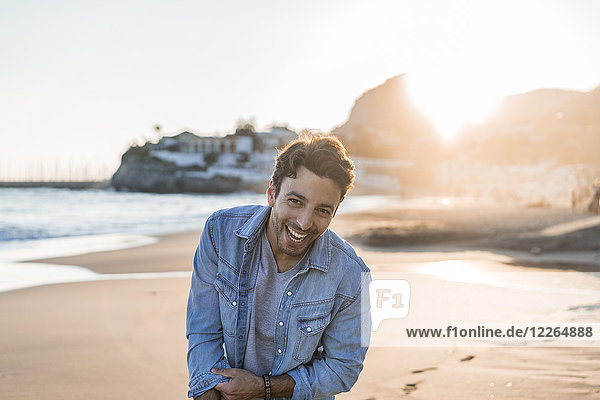 Portrait of laughing young man on the beach at sunset