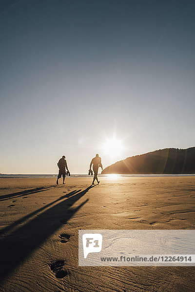 Canada  British Columbia  Vancouver Island  two men walking on beach at San Josef Bay at sunset