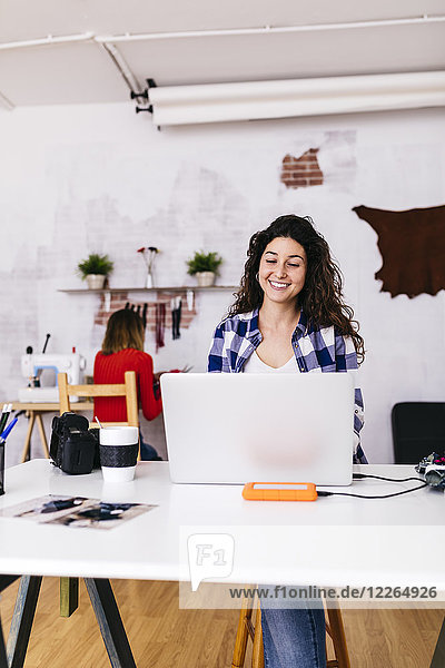 Smiling fashion designer using laptop in studio
