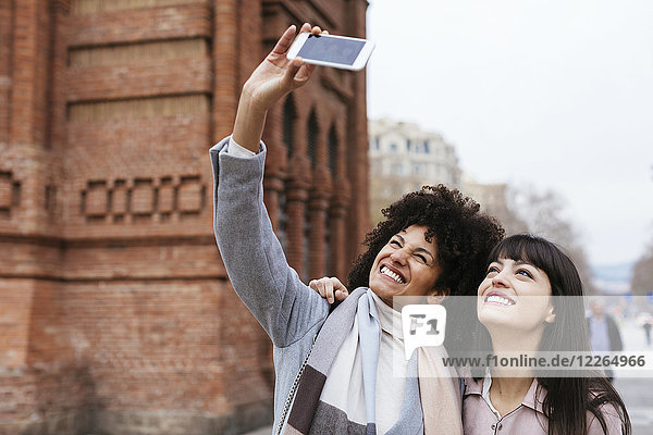 Spanien  Barcelona  zwei glückliche Frauen  die einen Selfie an einem Tor nehmen.