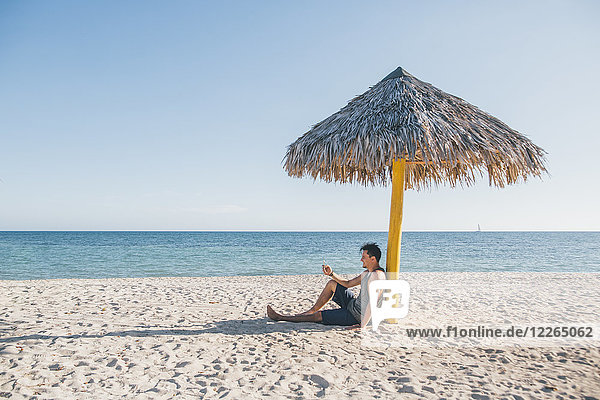 Cuba  Young man sitting under a sunshade at Playa Ancon