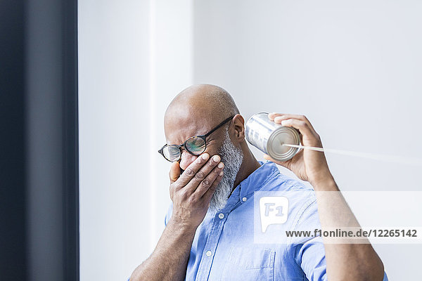 Laughing businessman with tin can phone in the office