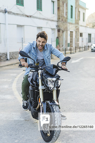 Porträt eines schreienden jungen Mannes  der auf einem Motorrad sitzt und lustige Gesichter zieht.