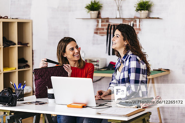 Two smiling fashion designers working in studio with laptop