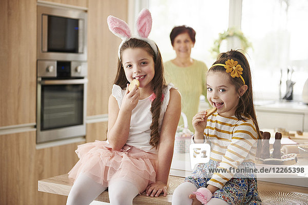 Portrait of two smiling girls eating cookies in kitchen