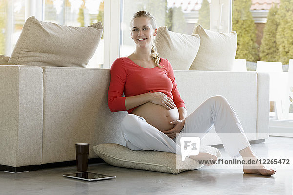 Porträt einer lächelnden schwangeren Frau  die zu Hause auf dem Boden sitzt