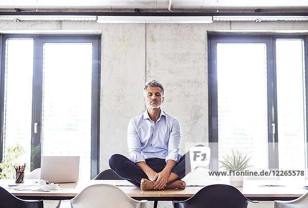 Mature businessman sitting barefoot on desk in office meditating