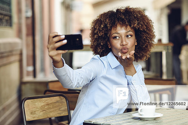 Frau mit Afro-Frisur sitzend im Outdoor-Café mit einem Selfie