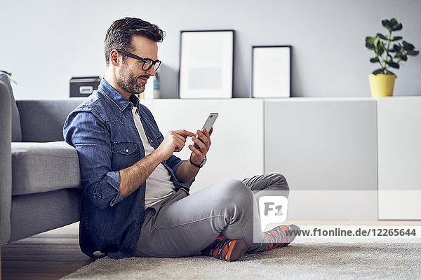 Smiling man sitting on floor in living room using cell phone