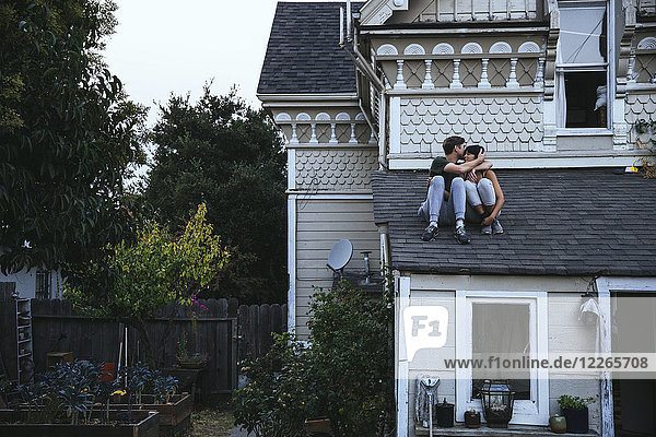 Paar auf dem Dach sitzend küssend