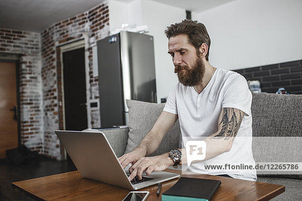 Bearded man sitting on the couch at home using laptop