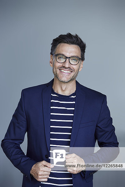 Porträt eines lachenden Geschäftsmannes mit Stoppel im blauen Anzugmantel und Brille