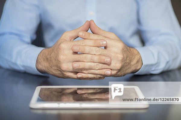 Man sitting at office desk with tablet folding hands