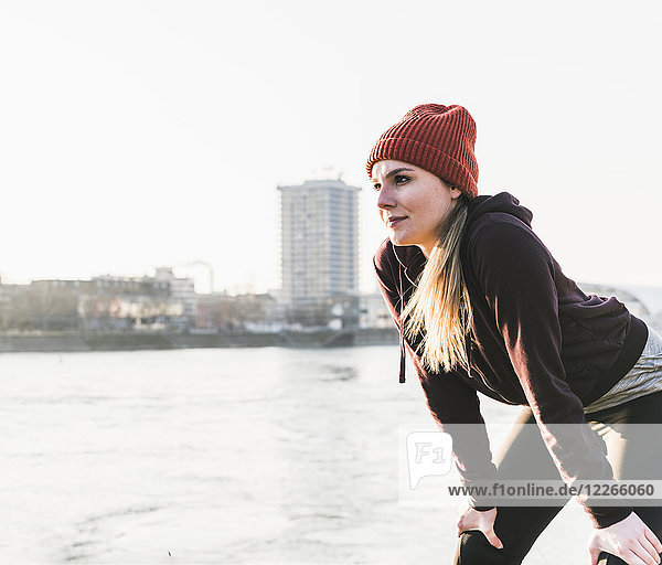 Sportliche junge Frau bei einer Pause am Flussufer in der Stadt