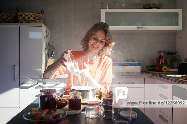 Lächelnde Frau macht Erdbeermarmelade in der Küche zu Hause
