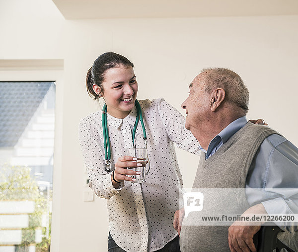Ein älterer Mann lächelt die Krankenschwester an  die zu Hause ein Glas Wasser hält.