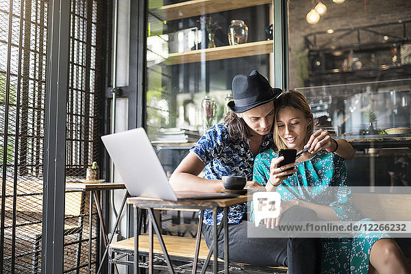 Künstlerpaar sitzt im Café und überprüft das Smartphone der jungen Frau
