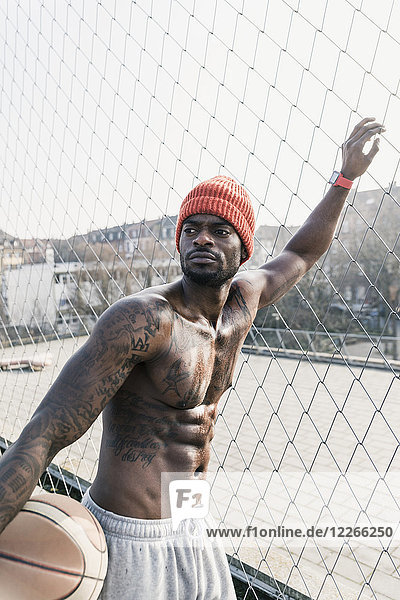 Portrait of muscular barechested basketball player standing at fence
