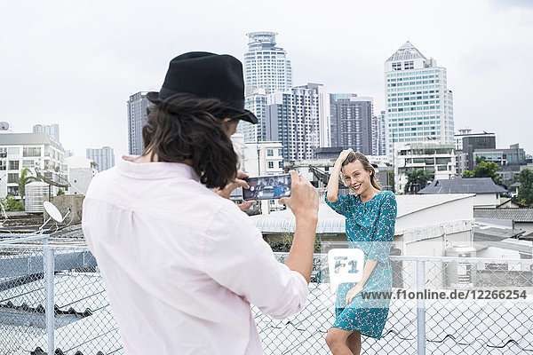TYoung Mann mit Smartphone beim Fotografieren der Freundin auf dem Dach