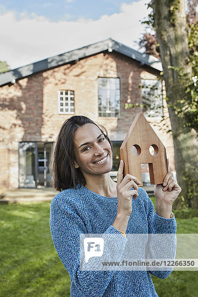 Portrait of smiling woman in garden of her home holding house model