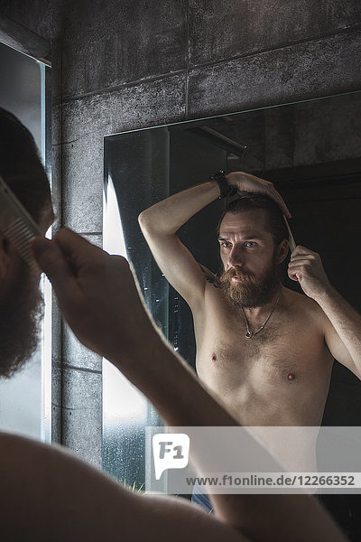Portrait of bearded man looking at his mirror image while combing his hair