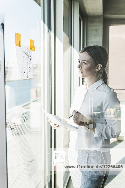 Young businesswoman looking at paper at the window