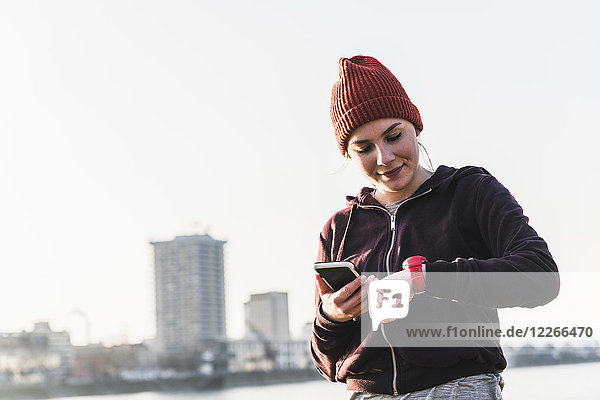Sportive young woman at the riverside in the city with smartphone and smartwatch