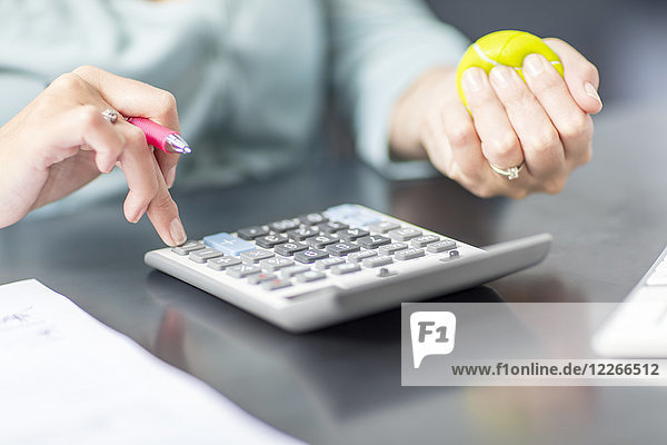 Woman at desk in office using calculator and stress ball