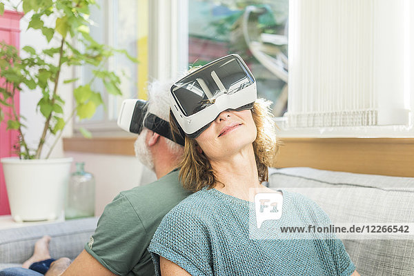 Erwachsenes Paar  das zu Hause auf der Couch sitzt und eine VR-Brille trägt.
